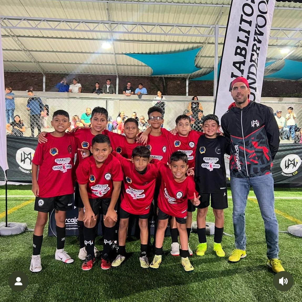 Grupo de niños futbolistas posando con un entrenador en un evento deportivo.